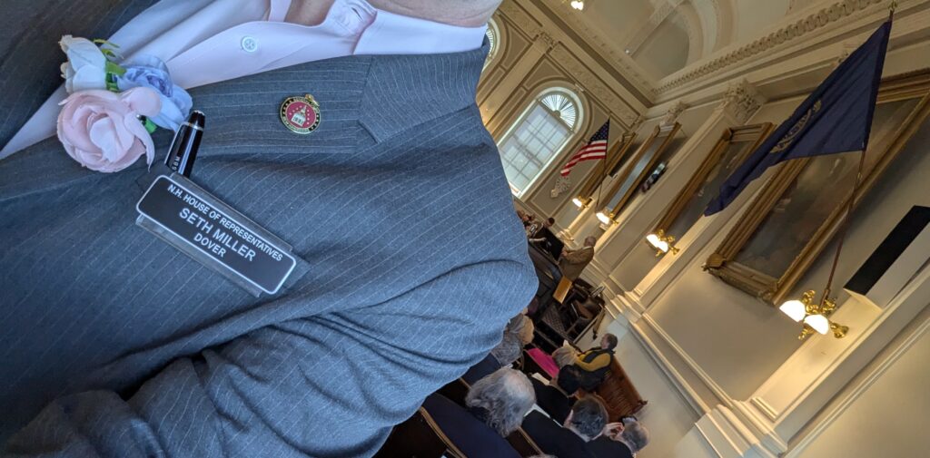 Pink, white, and blue flowers on my lapel, in support of trans rights, as I'm prepping to speak on the NH House floor.